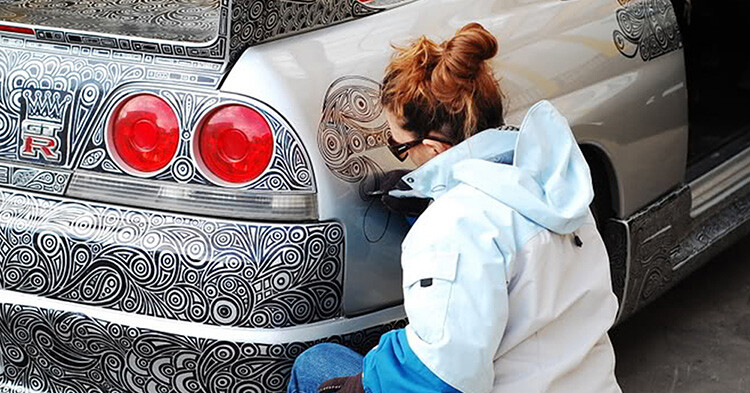 Un homme laisse sa femme artiste dessiner avec un stylo feutre sur sa Nissan Skyline GTR