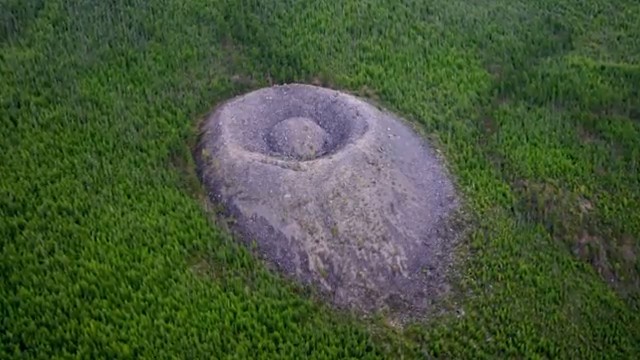Vue aérienne du cratère de Patomsky en Sibérie, ressemblant à un nid d'oiseau en roche avec un rocher arrondi en son centre.