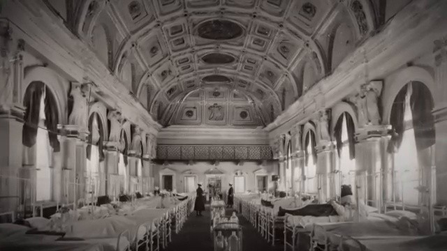 Intérieur d'une grande salle d'hôpital ancienne avec des lits alignés et des hauts plafonds voûtés.